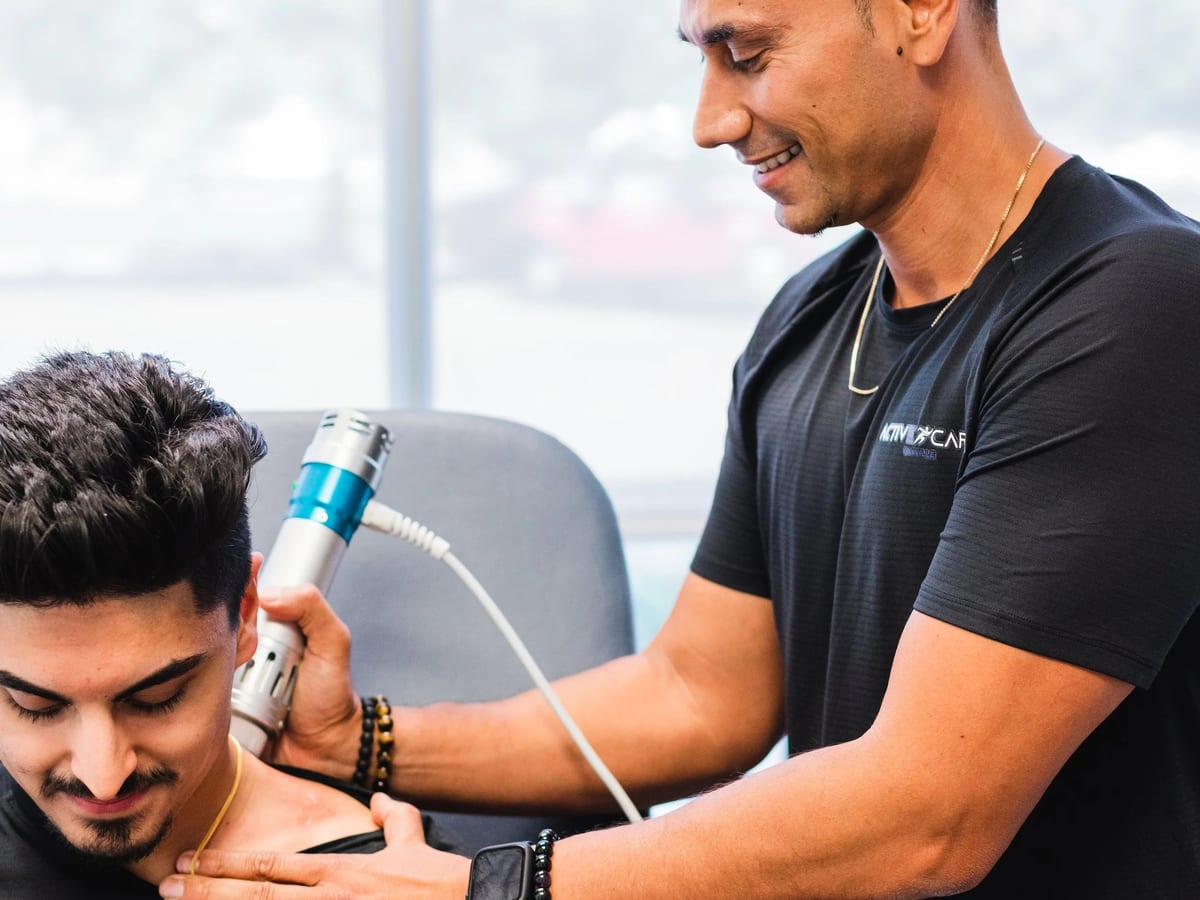 An Active Care Oakville practitioner treating a seated patient's shoulder with a handheld device